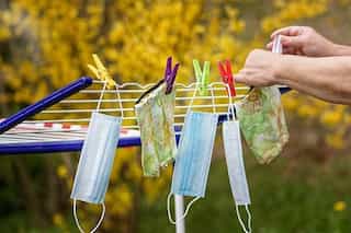 Hands hanging reusable cloth face masks outside to air dry